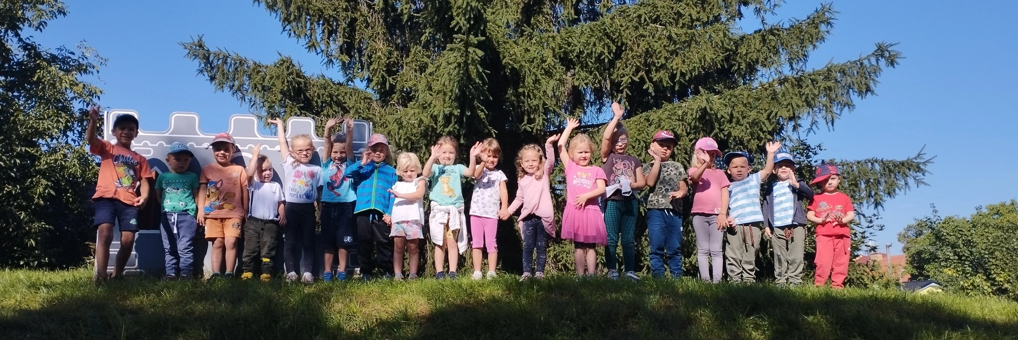 Mávající děti na kopečku na zahradě mateřské školy