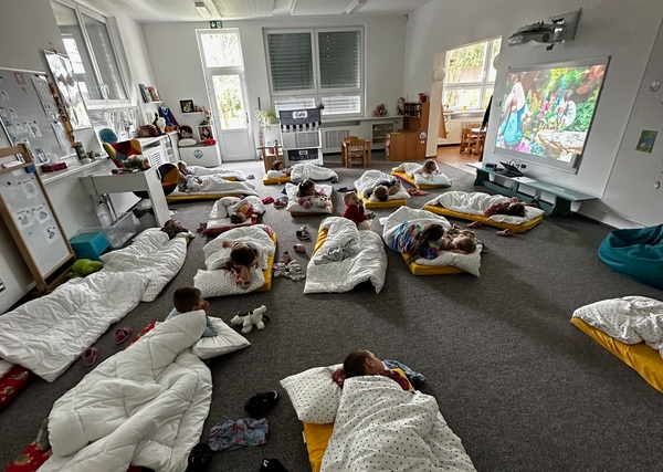 Náhledová fotka - Děti na koberci spící v postýlkách dívající se na pohádku