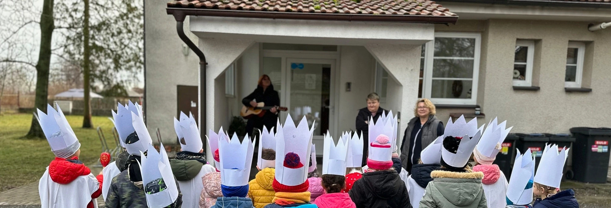 Děti s čepicemi před budovou