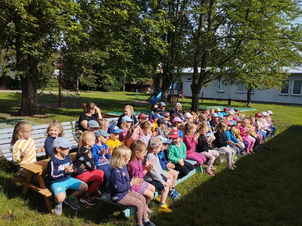 Náhledová fotka - Děti na zahradě školky sedící na lavičkách